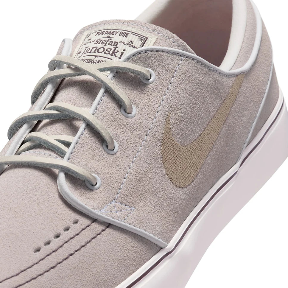 Light gray suede skate shoes with tan swoosh, lace-up front and white rubber sole