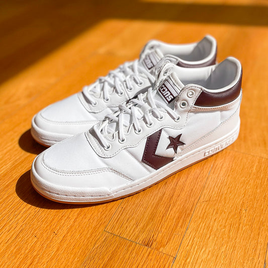 Pair of white mid-top lace-up sneakers with maroon side panel and star emblem on quarter.